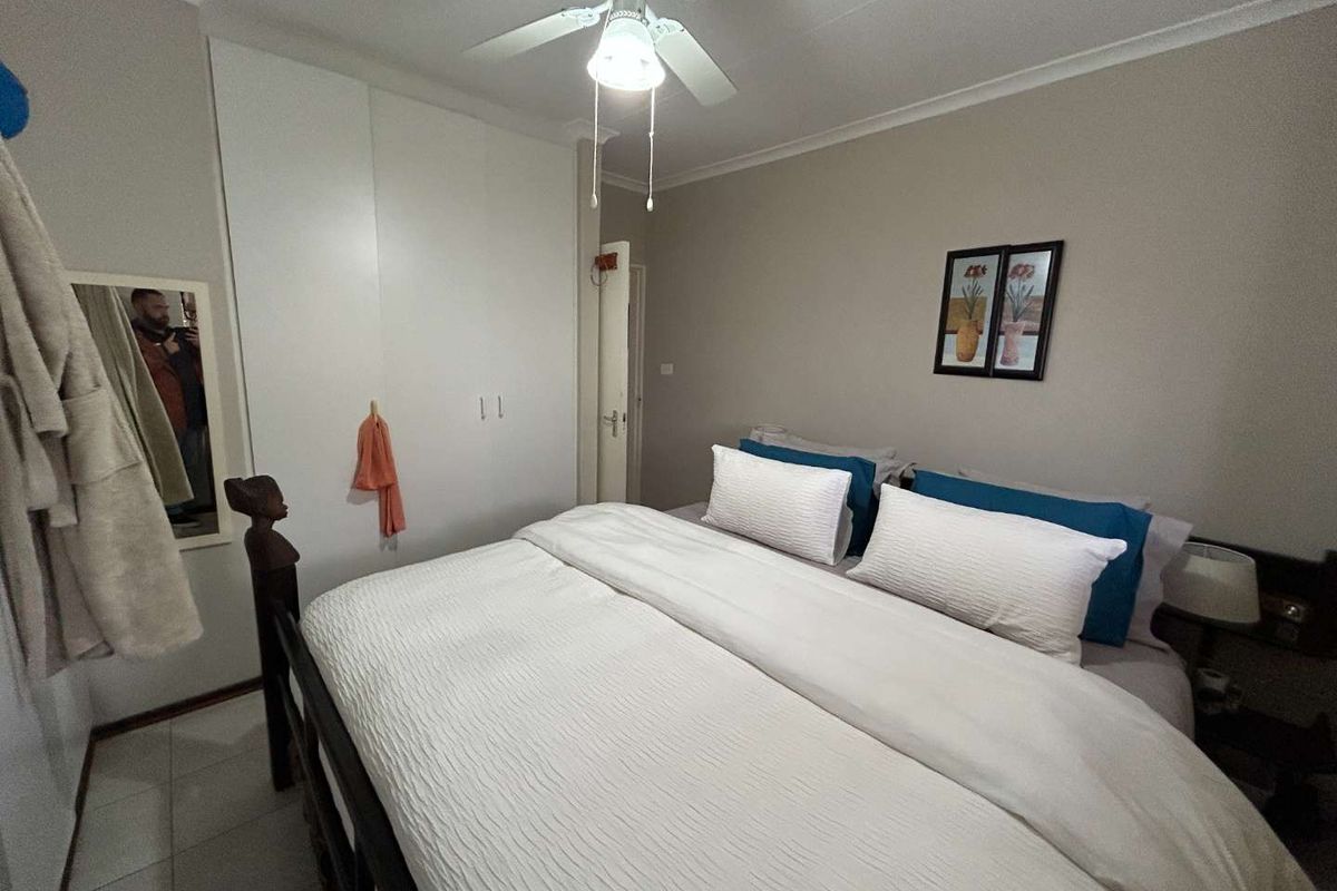 A well-maintained bedroom featuring built-in cupboards, a ceiling fan, and tiled flooring, offering a comfortable and functional living space.