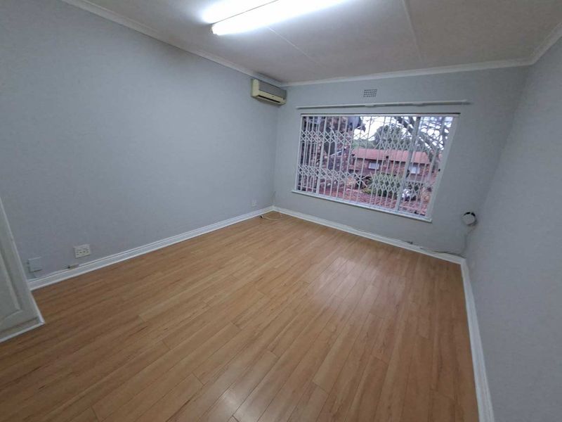 An empty bedroom featuring laminate flooring, an air conditioning unit, and a window fitted with a security gate.