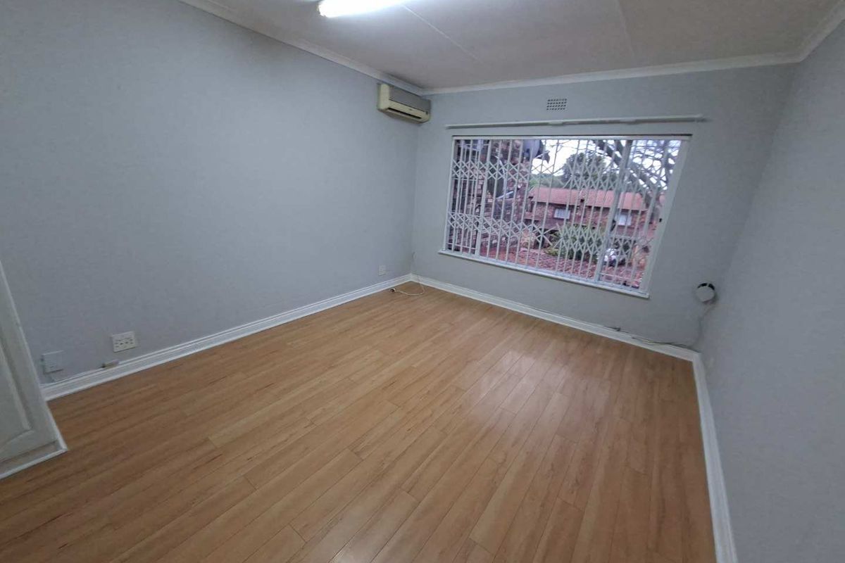 An empty bedroom featuring laminate flooring, an air conditioning unit, and a window fitted with a security gate.