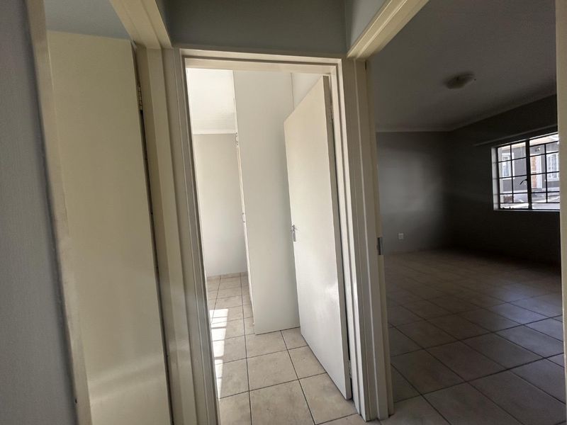 A view from the hallway looking into an empty bedroom with tiled flooring and built-in cupboards.