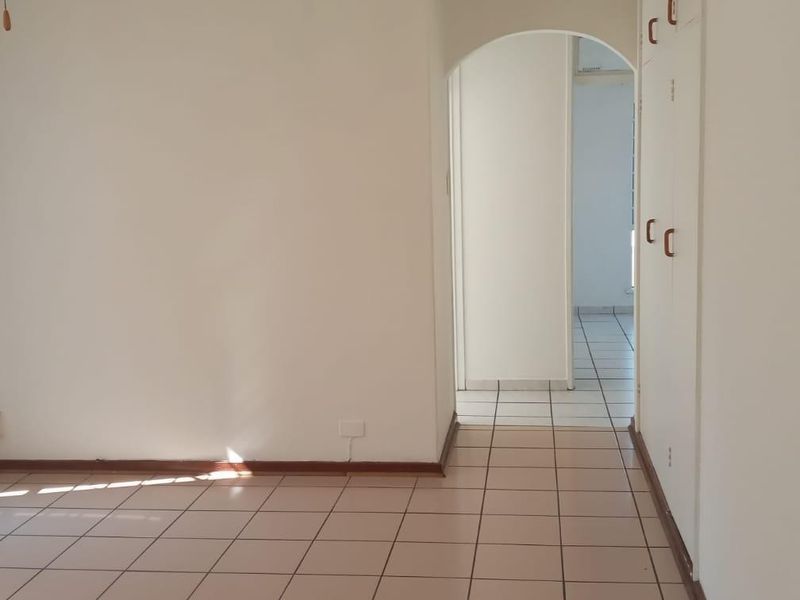 An empty living area featuring tiled flooring, built-in storage cupboards, and an arched entryway leading to an adjacent room.