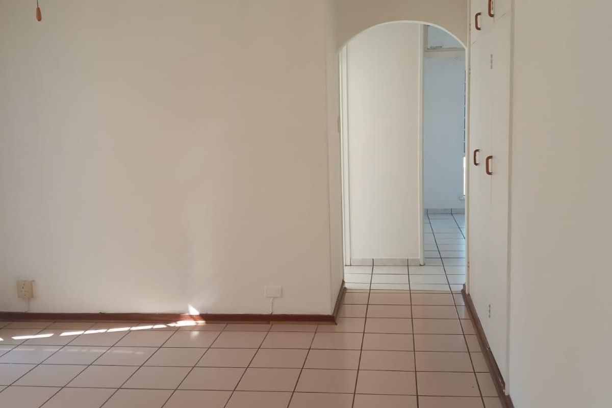 An empty living area featuring tiled flooring, built-in storage cupboards, and an arched entryway leading to an adjacent room.