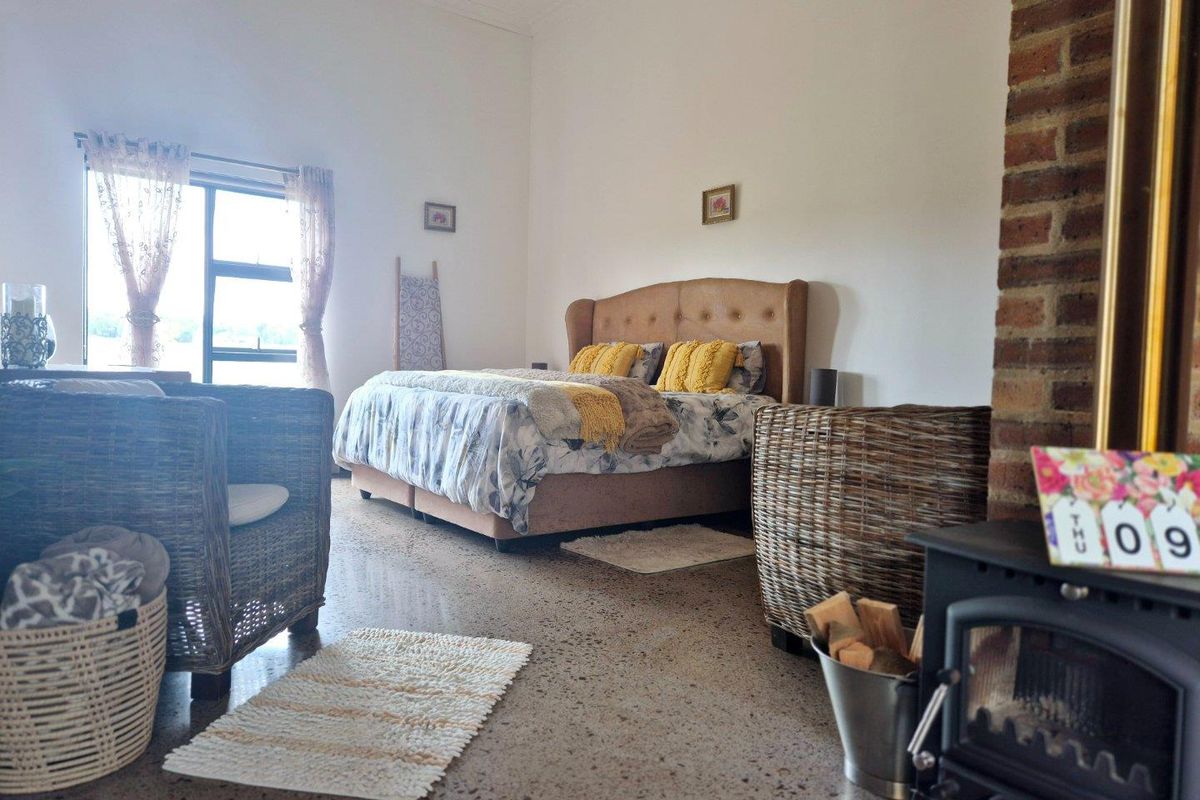 Spacious bedroom featuring polished concrete floors, a classic exposed brick fireplace with a wood-burning stove, and high ceilings with decorative cornicing.