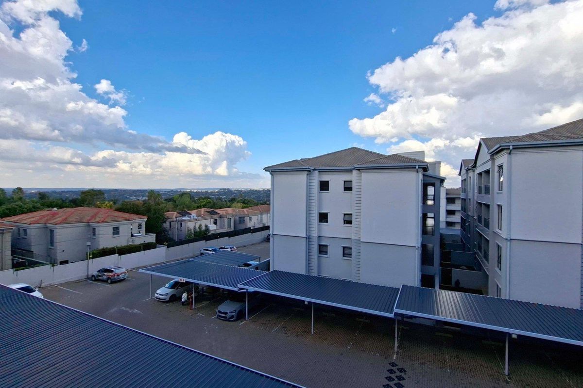 Aerial view of the apartment complex featuring covered parking bays, paved driveways, and surrounding residential buildings under a clear sky.