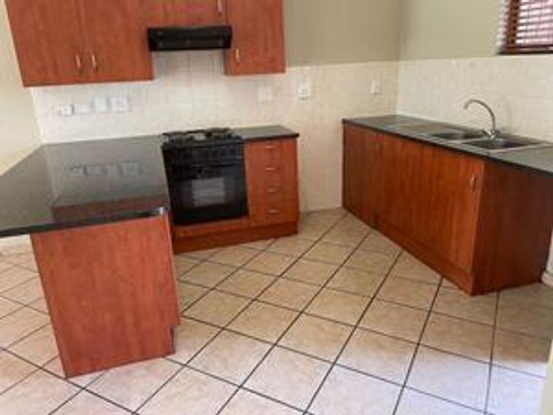 A functional kitchen featuring wooden cabinetry, granite countertops, a built-in oven with gas hob, and tiled flooring throughout.