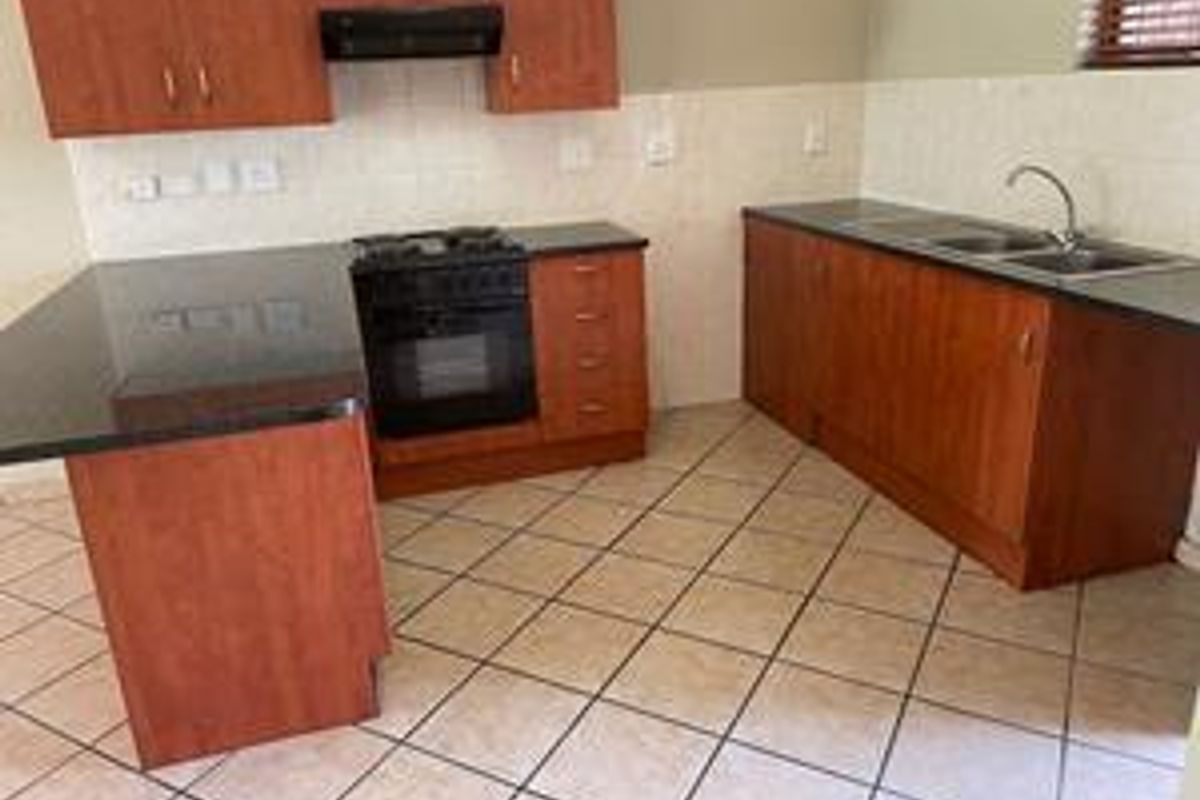 A functional kitchen featuring wooden cabinetry, granite countertops, a built-in oven with gas hob, and tiled flooring throughout.