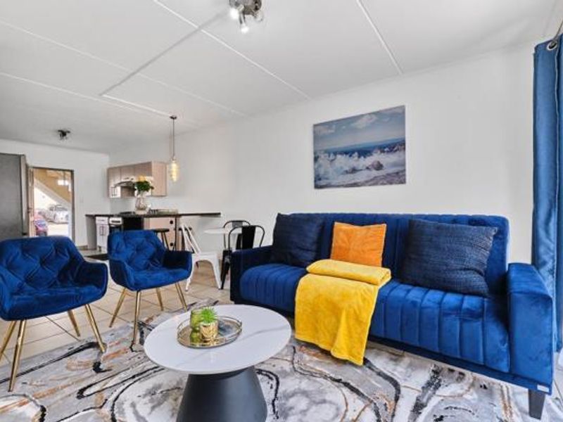 Open plan living area featuring a kitchen with built-in cabinetry and appliances, flowing into a comfortable lounge space with tiled flooring throughout.