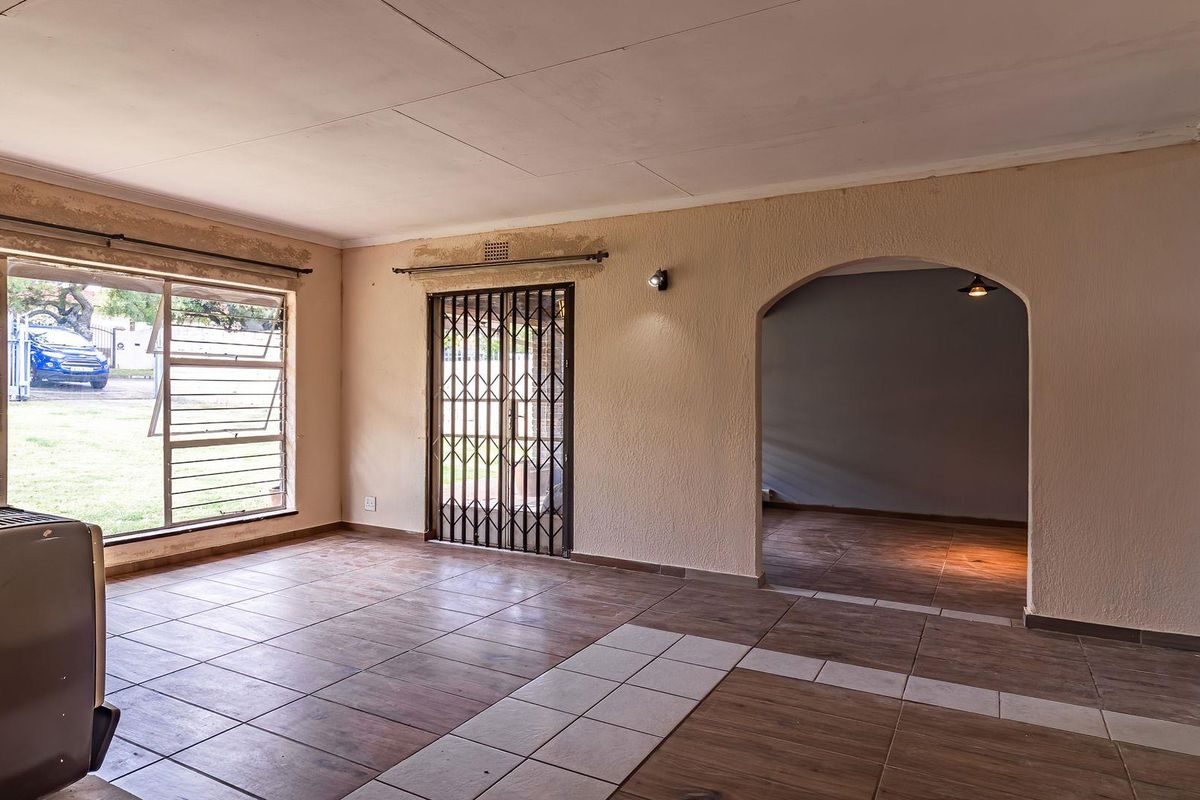 Spacious living area featuring tiled flooring, large windows, a security gate, and an arched entryway leading to an adjacent room.
