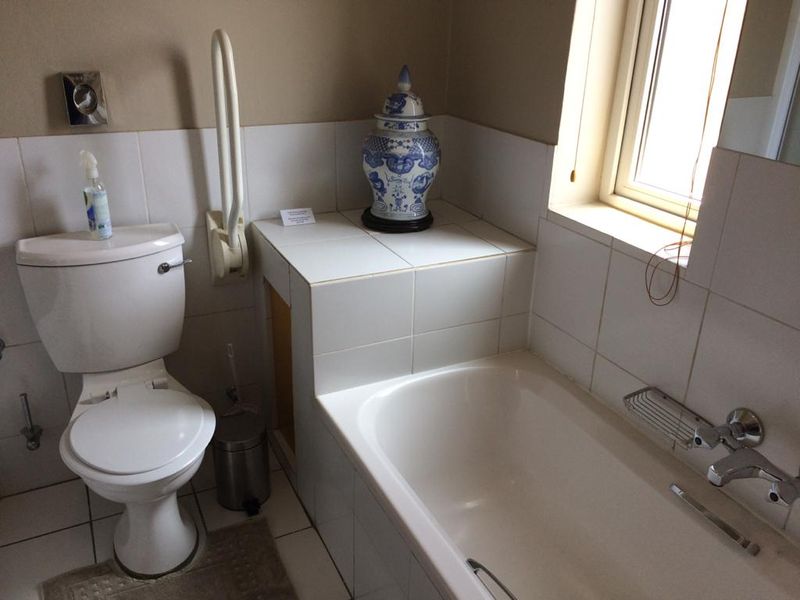 Functional bathroom featuring a standard toilet, bathtub with chrome fixtures, and tiled finishes, including a safety grab rail.
