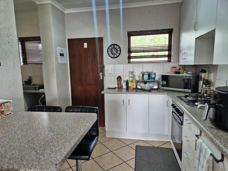 A functional kitchen featuring built-in cabinetry, granite countertops, a gas hob, and an integrated oven, with tiled flooring and natural light.