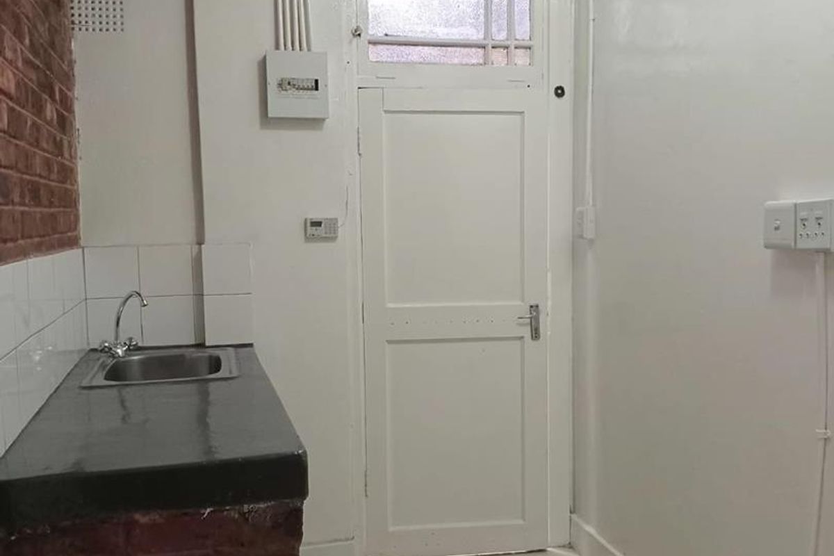 A compact kitchen area featuring a brick-base counter with a stainless steel sink, tiled flooring, and exposed electrical infrastructure.