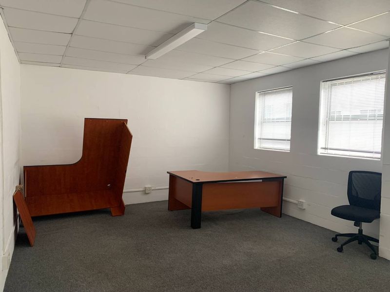 A functional office space featuring carpeted flooring, a suspended ceiling with integrated lighting, and dual windows fitted with venetian blinds.