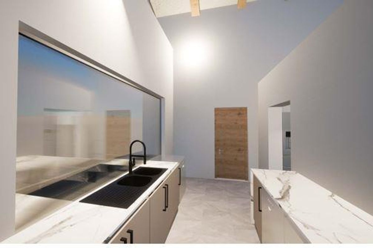 A modern kitchen featuring marble-look countertops, sleek cabinetry, a black sink with a contemporary faucet, and high vaulted ceilings with exposed beams.
