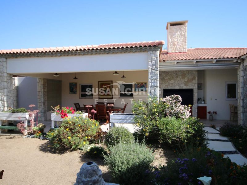 A covered outdoor patio area featuring stone cladding, a built-in braai, and direct access to the garden and paved pathways.