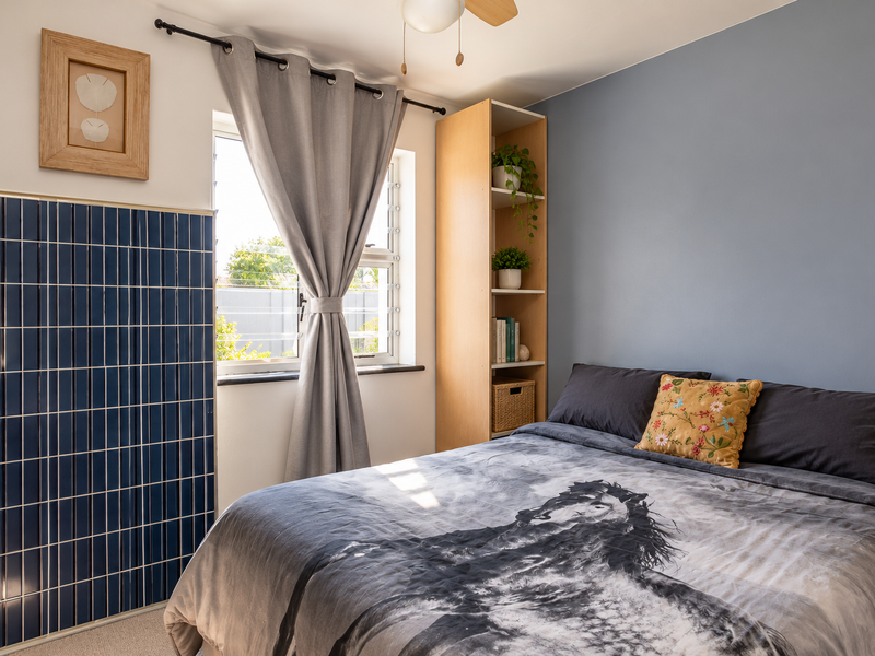 A well-lit bedroom featuring a blue tiled accent wall, built-in shelving, and a louvered window with natural light.