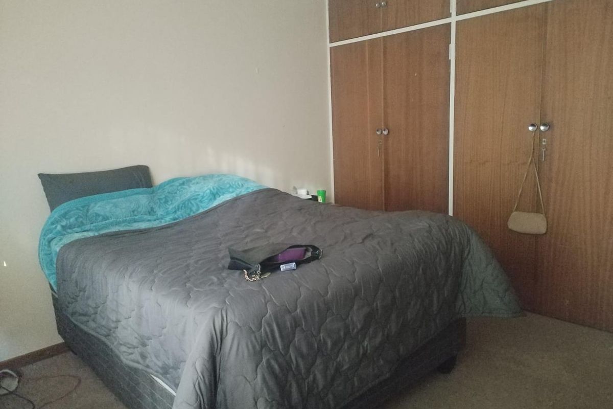 A functional bedroom featuring built-in wooden cupboards and carpeted flooring, offering a neutral space ready for personalization.