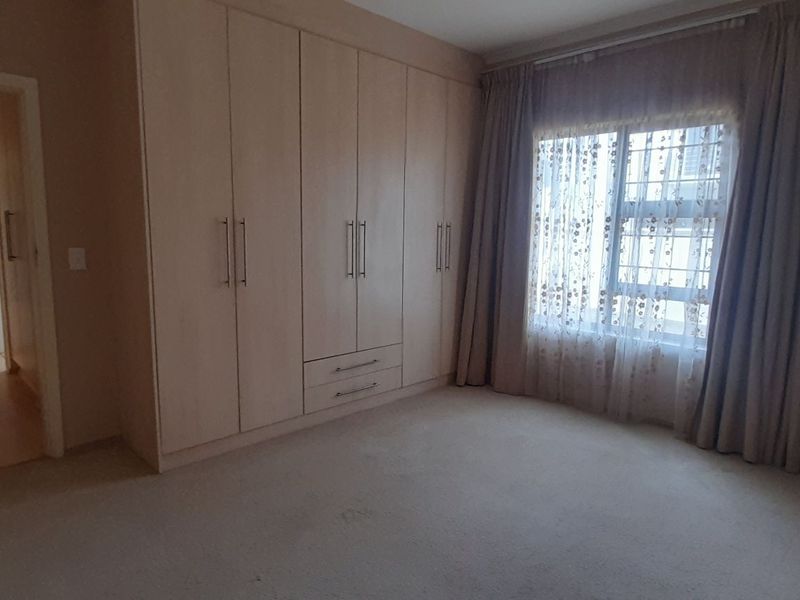 A spacious bedroom featuring neutral carpeted flooring and extensive built-in wooden cupboards, offering ample storage space and a bright, functional layout.