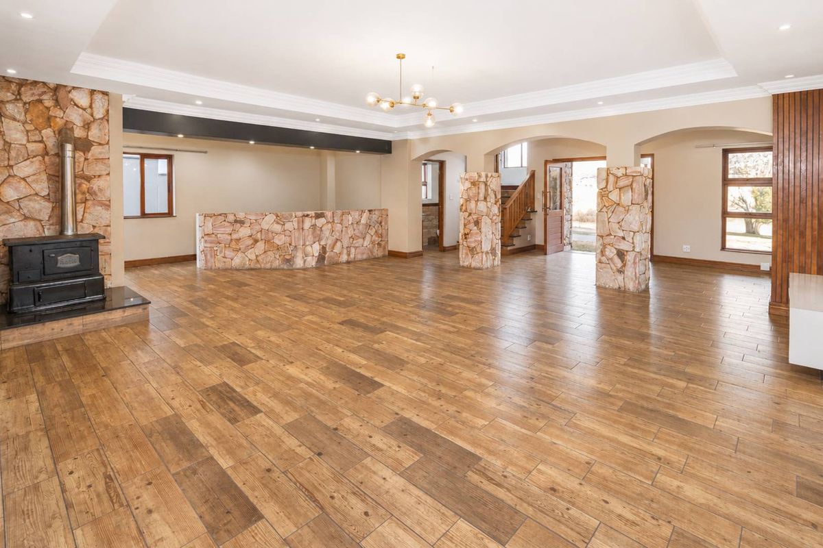 Spacious open-plan living area featuring a stone fireplace, wood-burning stove, stone pillars, and timber-look tile flooring with elegant crown molding.