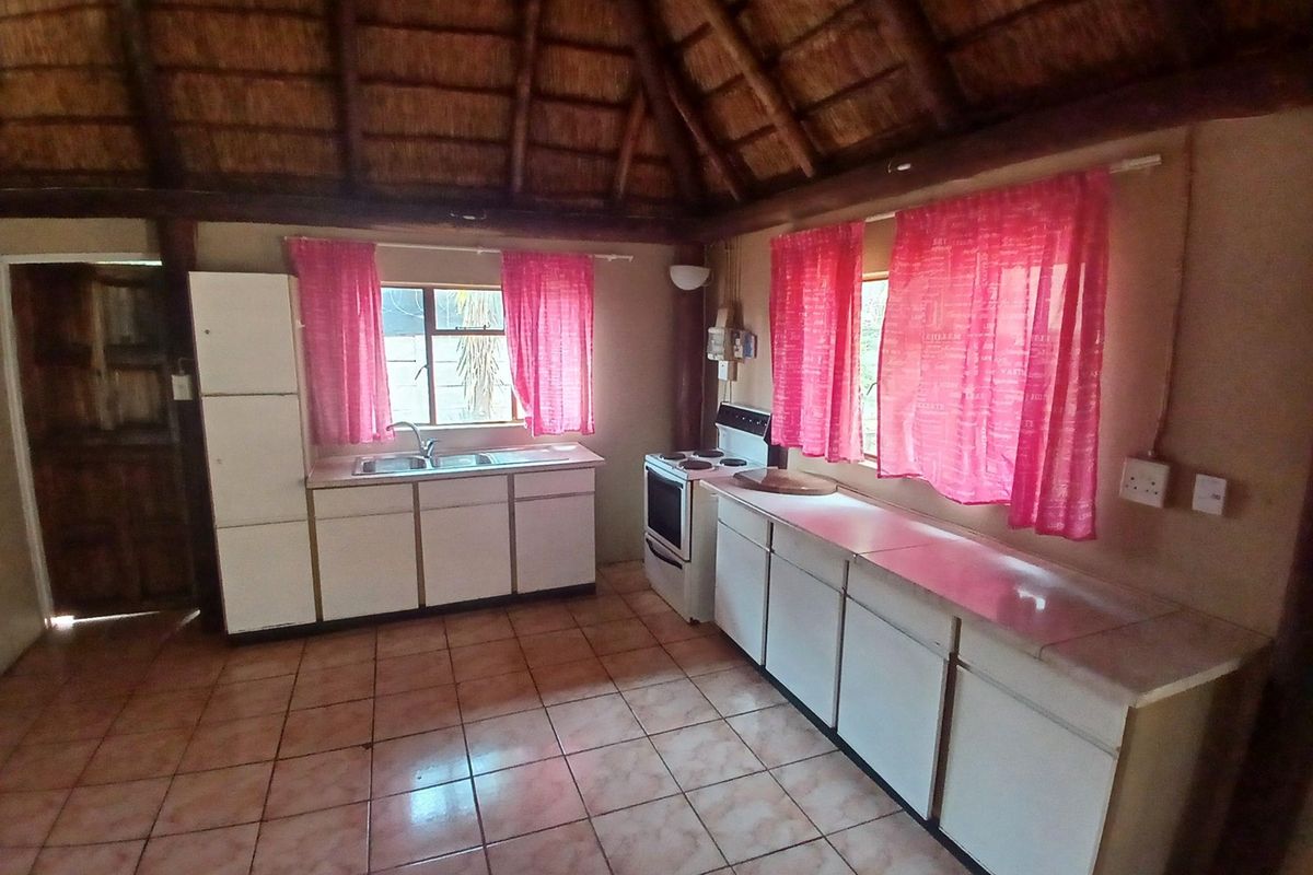 A rustic kitchen featuring a traditional thatched ceiling, tiled flooring, built-in cabinetry, and a freestanding stove, offering a unique character-filled space.