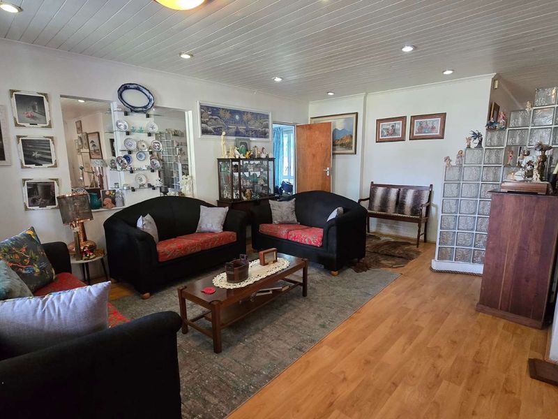 A spacious living room featuring laminate flooring, a timber tongue and groove ceiling, recessed downlights, and a decorative glass block partition.