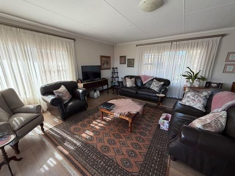 A spacious living room featuring laminate flooring and large windows with curtain treatments, offering a comfortable and well-lit area for relaxation.