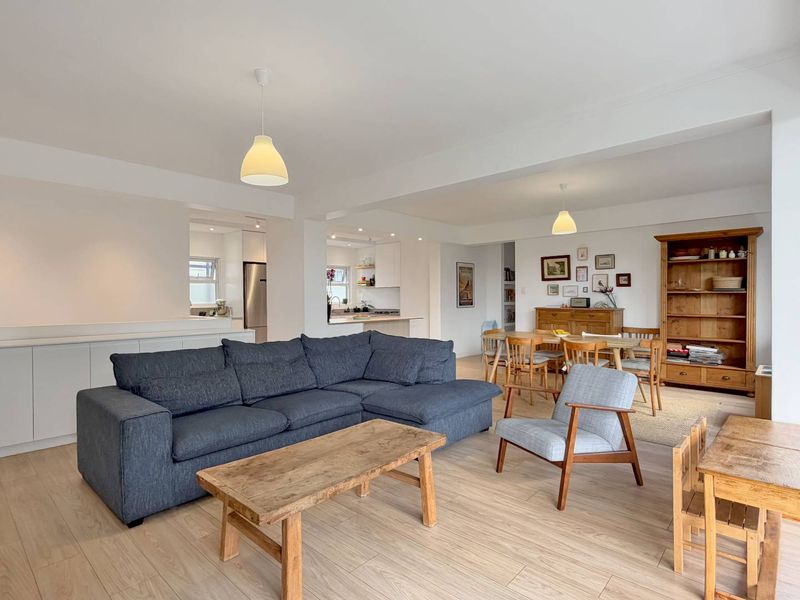 Spacious open-plan living and dining area featuring light wood-look laminate flooring, neutral walls, and a seamless transition into the modern kitchen space.