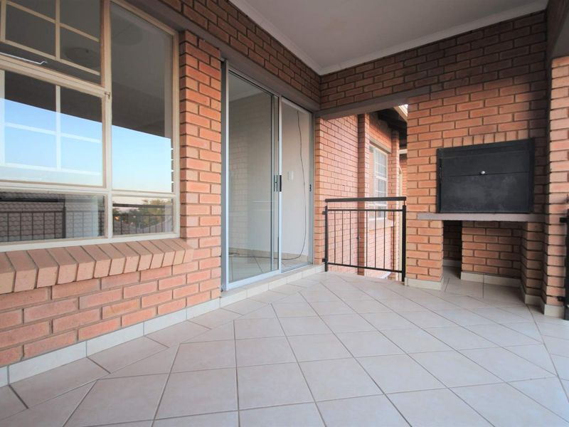 Covered balcony featuring exposed brick walls, tiled flooring, a built-in braai, and sliding door access to the interior living space.