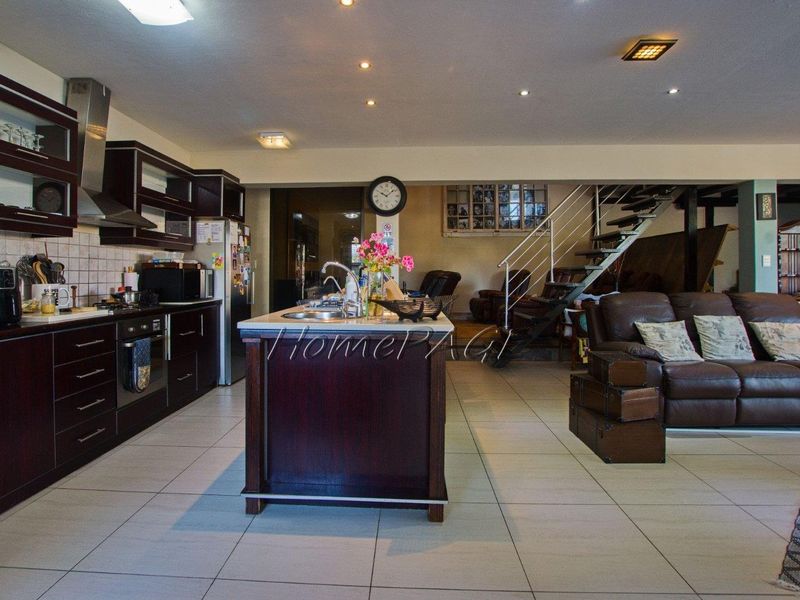 Spacious open-plan living area featuring a modern kitchen with dark cabinetry, a central island, and an integrated staircase leading to the upper level.
