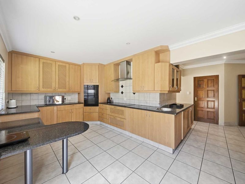 A spacious kitchen featuring light wood cabinetry, granite countertops, built-in oven, extractor fan, and tiled flooring, offering a functional layout with ample storage space.