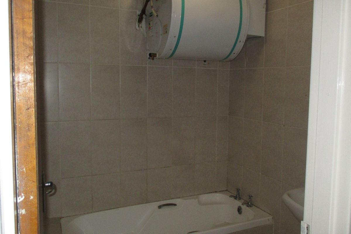 A compact bathroom featuring a built-in bathtub, tiled walls, and a wall-mounted electric geyser.