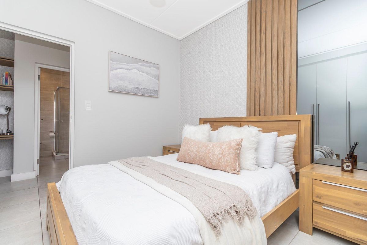Modern bedroom featuring a feature wall with vertical timber slats, built-in mirrored wardrobes, and an en-suite bathroom with a glass-enclosed shower.