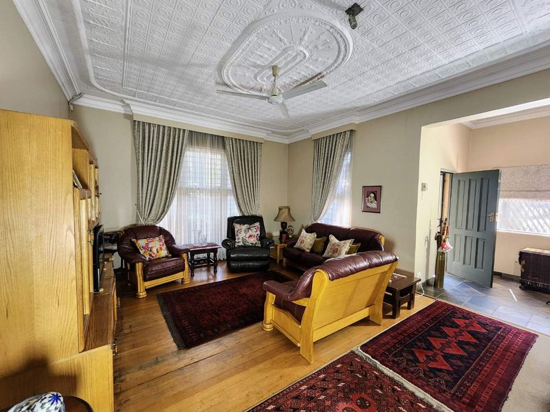 A spacious living room featuring original pressed metal ceilings with a decorative rose, ceiling fan, and polished timber flooring.