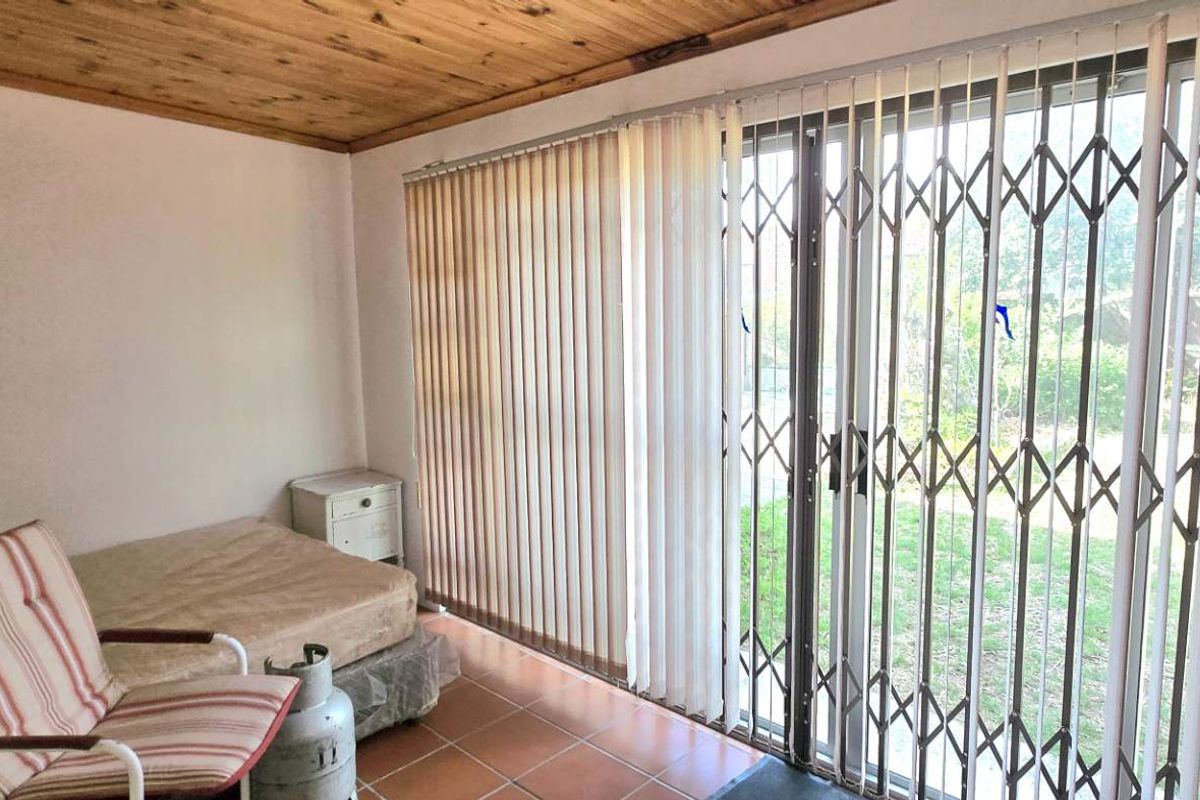 A bedroom featuring a timber-clad ceiling, tiled flooring, and large sliding glass doors with security gates providing direct access to the garden.