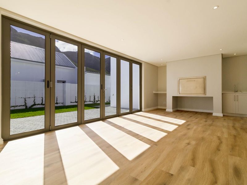 Spacious living area featuring modern laminate flooring, built-in braai, and large aluminium stacker doors opening to the garden.