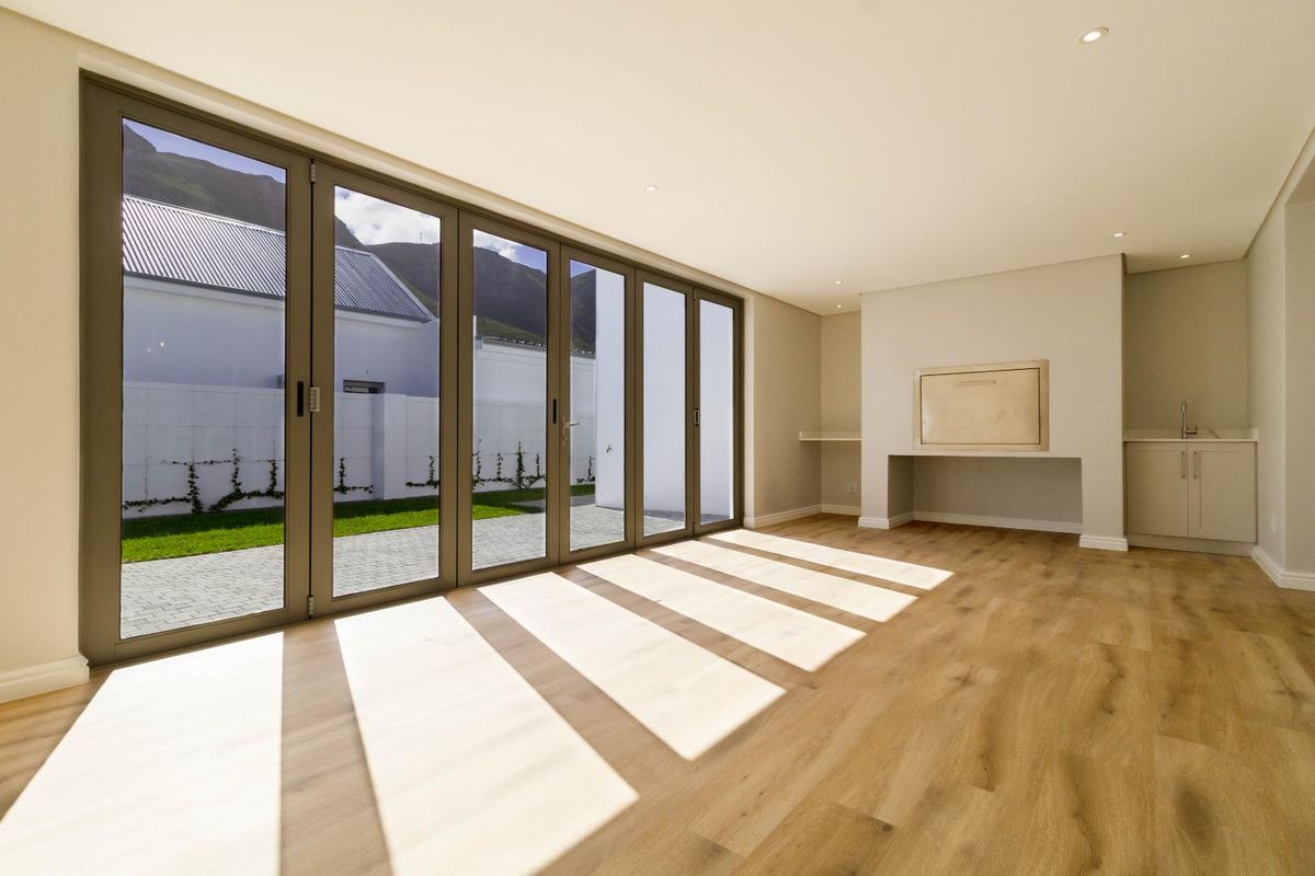 Spacious living area featuring modern laminate flooring, built-in braai, and large aluminium stacker doors opening to the garden.