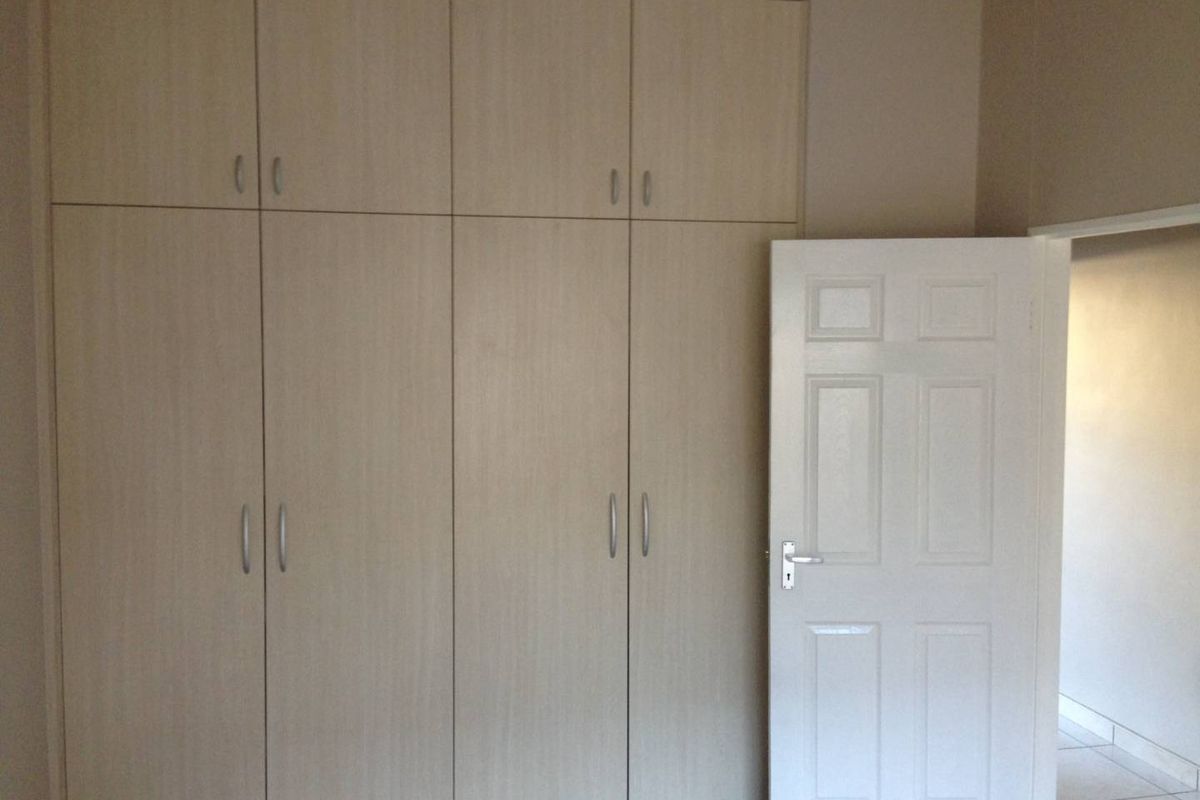 A bedroom featuring light wood-finish built-in cupboards and a white panel door, providing ample storage space in a clean, neutral setting.