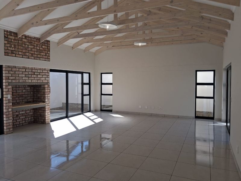 Spacious open-plan living area featuring high vaulted ceilings with exposed timber trusses, a feature brick fireplace, and large sliding doors leading outdoors.