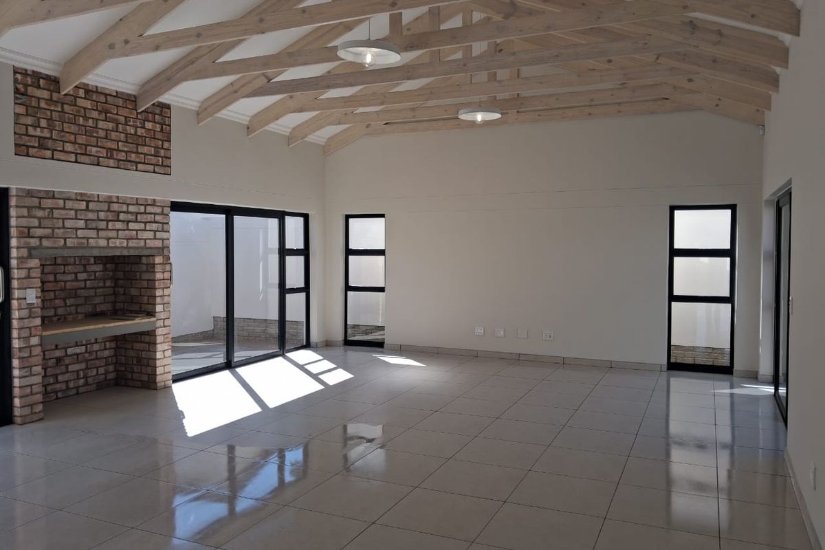 Spacious open-plan living area featuring high vaulted ceilings with exposed timber trusses, a feature brick fireplace, and large sliding doors leading outdoors.