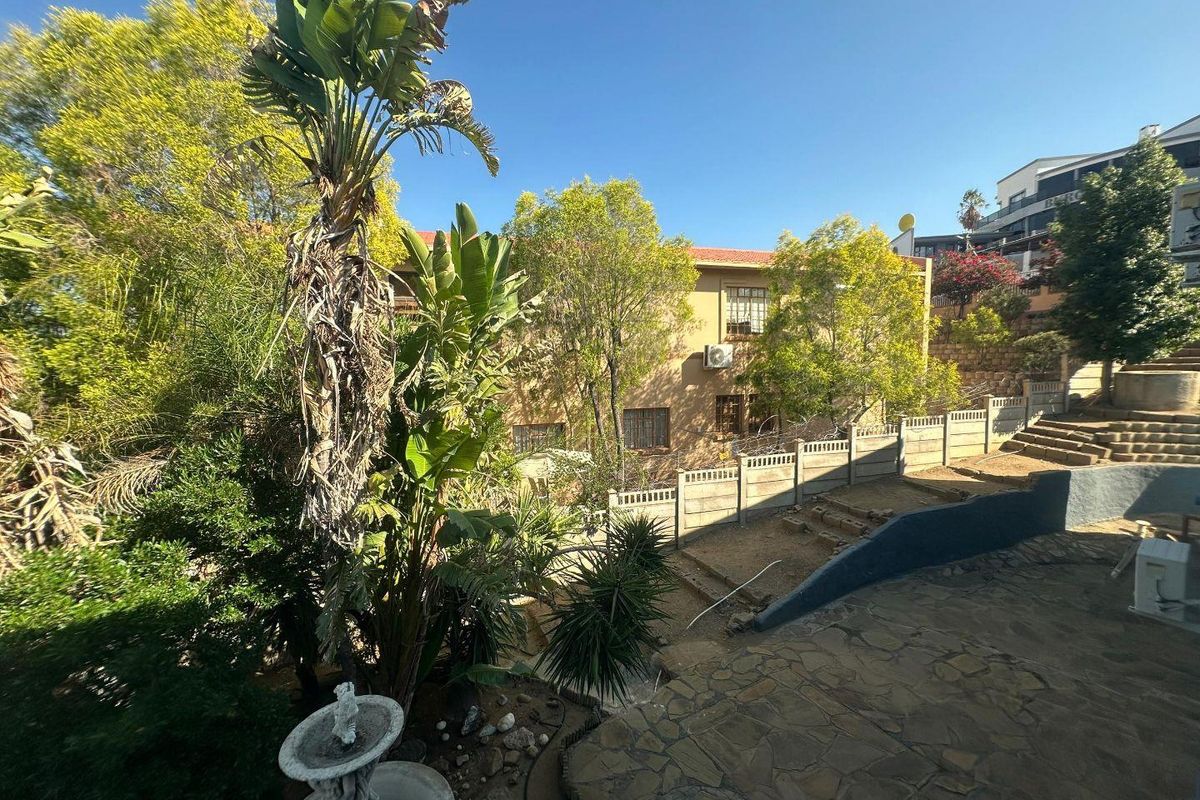 A view of the rear exterior of the office building, featuring a stone-paved patio area, tiered garden landscaping, and perimeter walling.