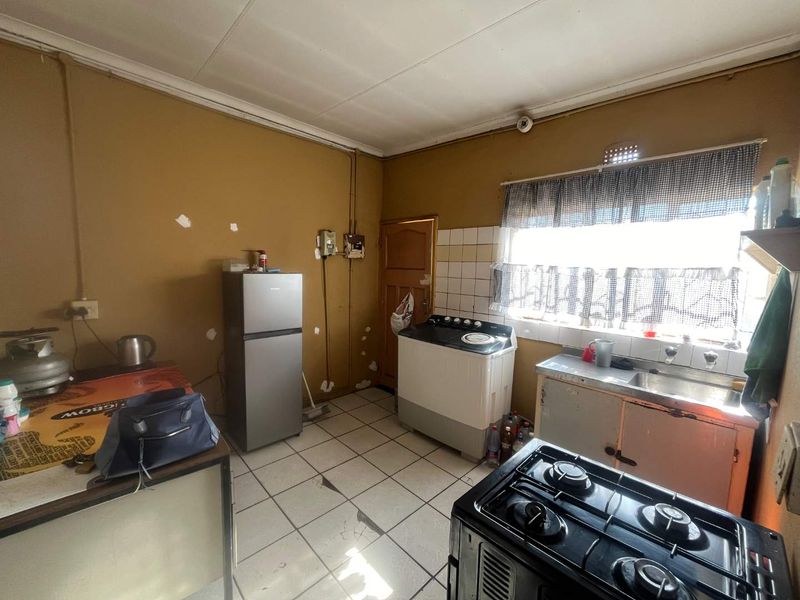 A functional kitchen space featuring tiled flooring, a stainless steel sink, and built-in cabinetry, currently requiring cosmetic updates and wall repairs.