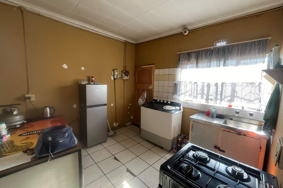 A functional kitchen space featuring tiled flooring, a stainless steel sink, and built-in cabinetry, currently requiring cosmetic updates and wall repairs.