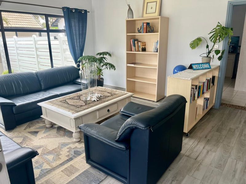 A bright living room featuring large windows, wood-look flooring, and neutral wall finishes, providing a comfortable and functional space.