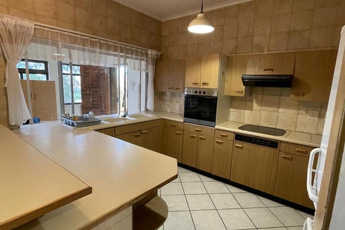 A functional kitchen featuring wooden cabinetry, built-in oven and hob, tiled flooring, and a breakfast bar counter.