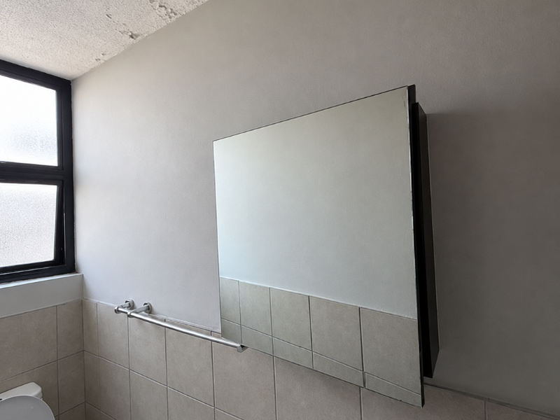A functional bathroom featuring a wall-mounted mirror cabinet, ceramic basin, and tiled walls, currently showing signs of ceiling wear requiring maintenance.
