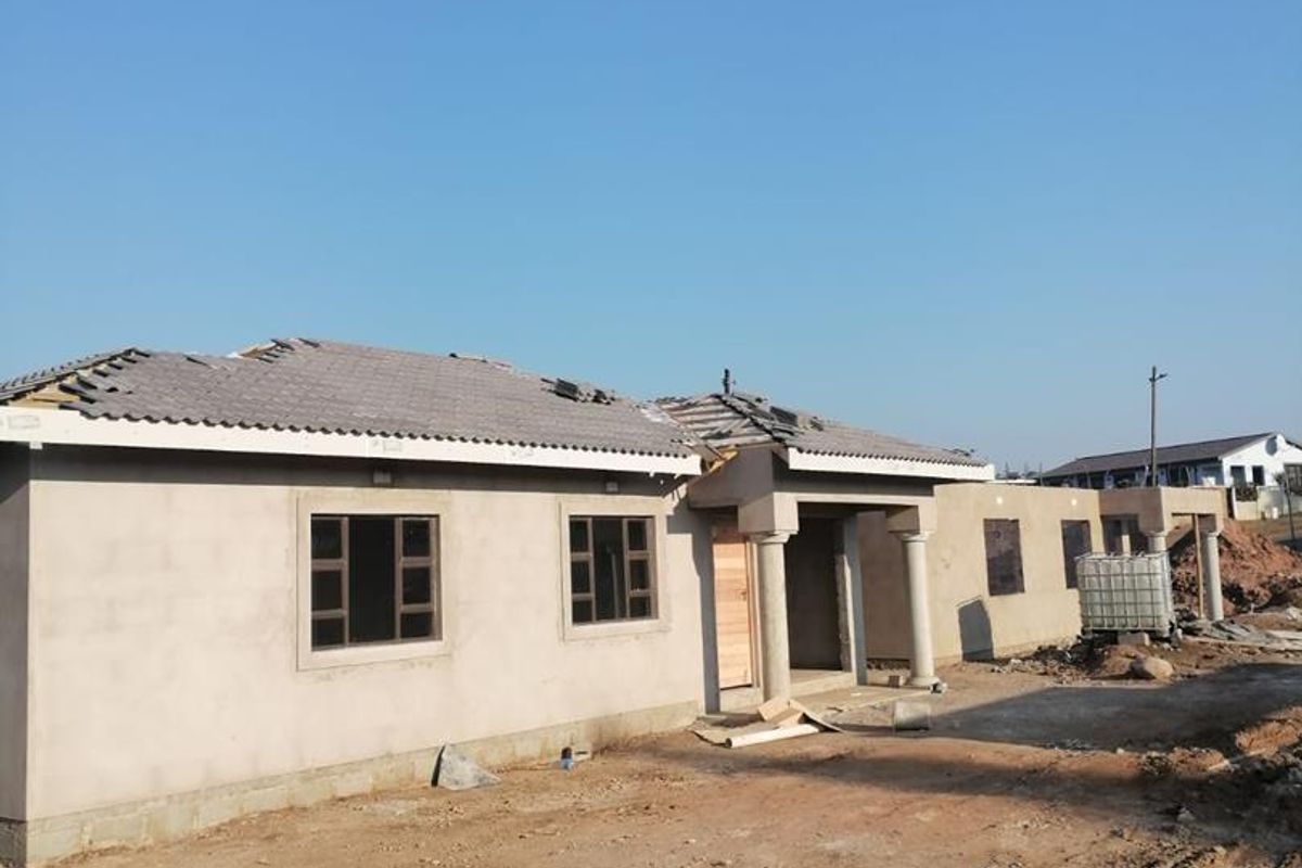 Exterior view of a townhouse under construction, featuring plastered walls, aluminium windows, and an incomplete roof structure on a site requiring landscaping.