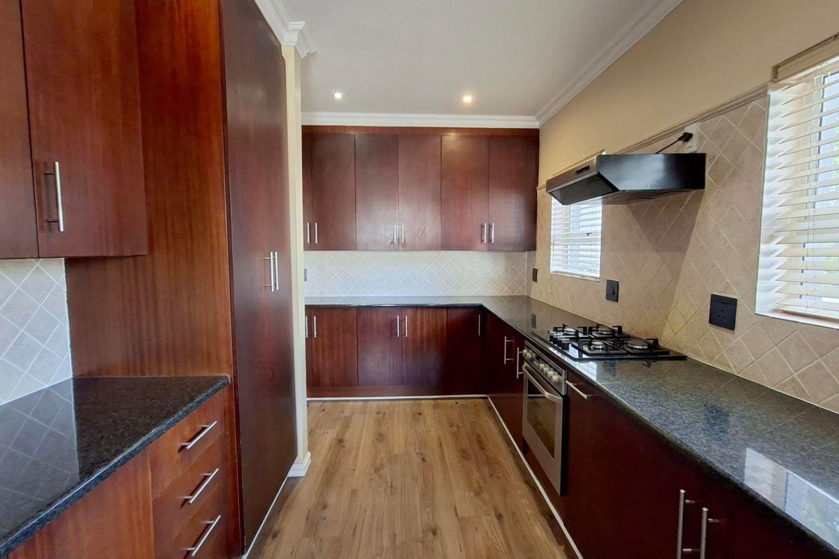 A well-maintained kitchen featuring dark wood cabinetry, granite countertops, a gas hob, built-in oven, and modern laminate flooring.