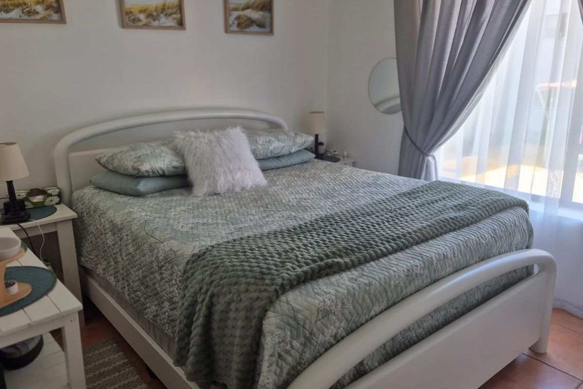 A cozy bedroom featuring tiled flooring and a large window with curtains, providing natural light and a comfortable living space.