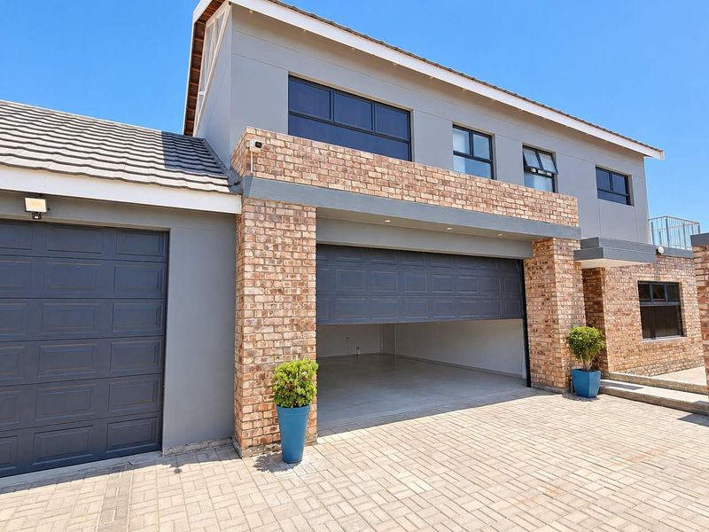 Modern double-storey house exterior featuring a double garage, face-brick accents, and a paved driveway under a clear blue sky.