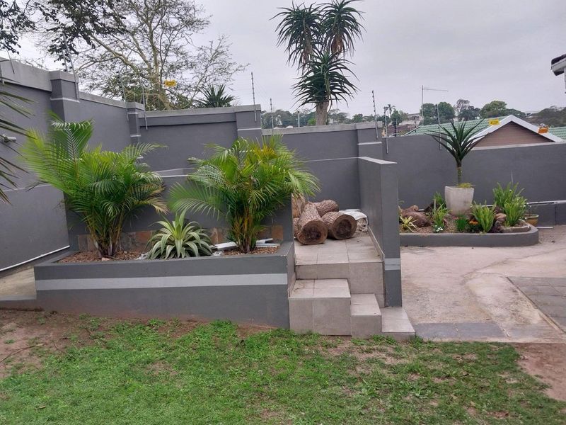 A landscaped rear garden area featuring raised garden beds, tiled steps, and a high perimeter wall with integrated electric fencing.