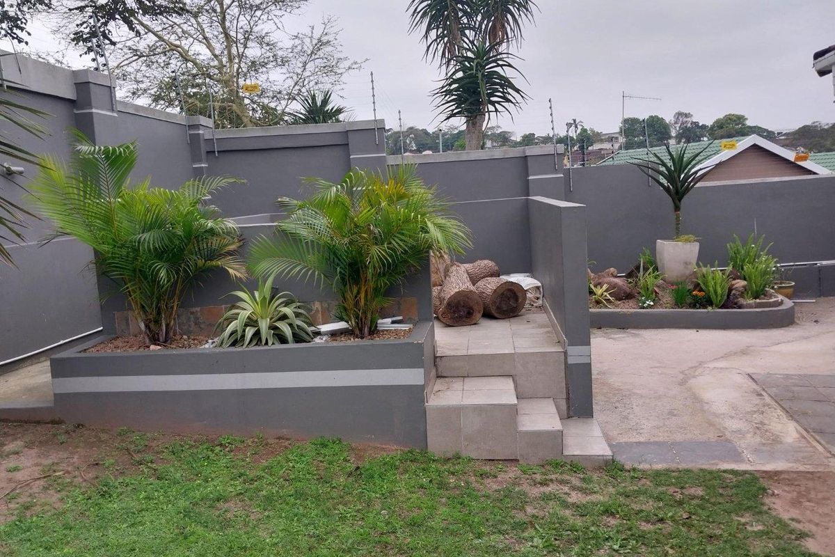 A landscaped rear garden area featuring raised garden beds, tiled steps, and a high perimeter wall with integrated electric fencing.